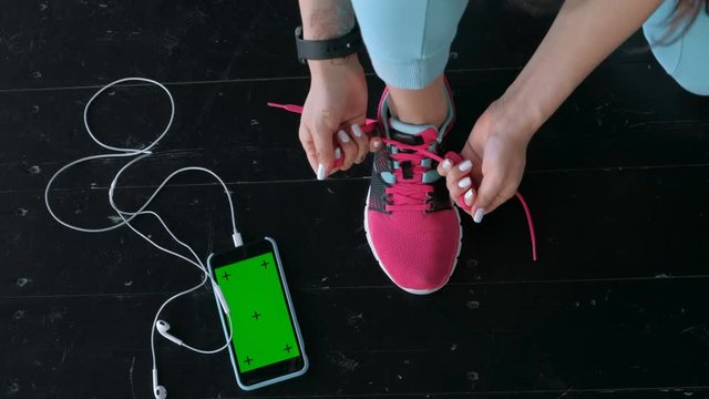 Sporty woman holding phone with empty screen sitting on the sunbed with jump rope, gloves and drink bottle on background 20s 4k