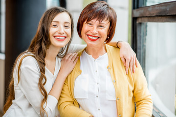 Portrait of a smiling mother and daughter standing together indoors near the window