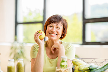 Fototapeta premium Portrait of a beautiful older woman with green healthy food on the table indoors on the window background