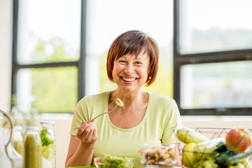 Portrait of a beautiful older woman with green healthy food on the table indoors on the window...