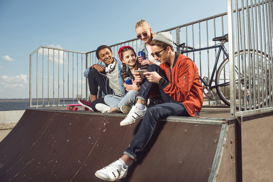 teenagers having fun with smartphone in skateboard park, hipster students concept