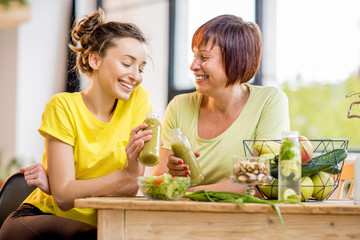 Young and older women sitting with healthy food and fresh drinks after the sports training indoors...