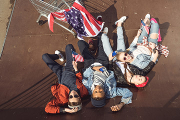 Fototapeta na wymiar elevated view of teenagers having fun and lying with american flag in skateboard park, hipster style concept