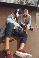 Obraz na płótnie Canvas hipster couple listening music with headphones and siiting in skateboard park, teenagers having fun concept