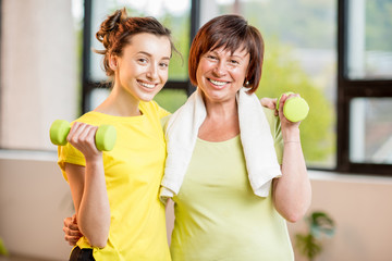 Young and older women in sportswear training with dumbbells indoors on the window background