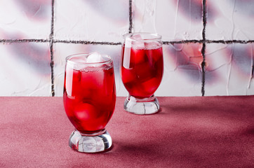 Cold cherry drink with ice cubes in glasses, on pink background