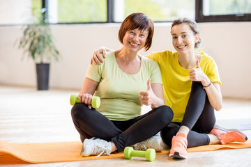 Portrait of a mother and daughter in sports wear sitting together after the training indoors