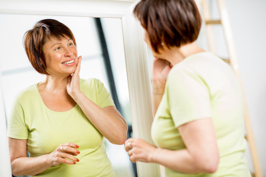Beautiful older woman looking at her face with a smile into the mirror