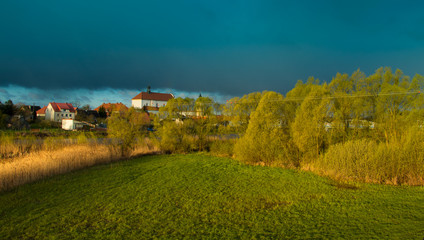 zielona łąka z wiosennymi zaroślami i białym klasztorem w oddali