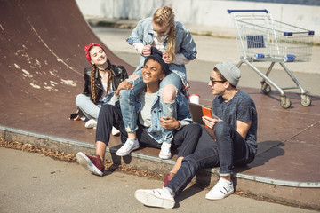 Teenagers group sitting together on the ramp and having fun at skateboard park