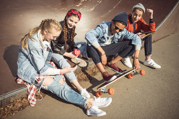 Teenagers group sitting sitting together and using digital devices at skateboard park