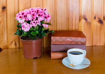 Books, cup of coffee and pelargonia flower on wooden table over wooden background