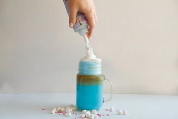 Girl is adding cream in cup of colored blue milk. Milk shake, cocktaill, frappuccino.  Unicorn...