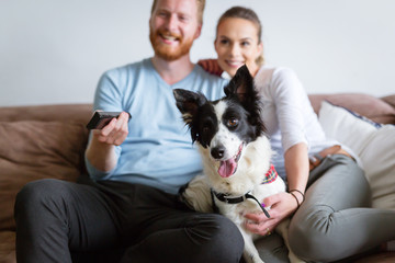 Beautiful couple watching television at home with their dog