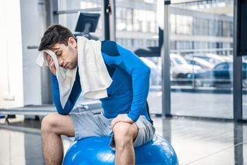 Tired young man resting on fitness ball at gym