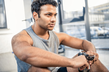 Handsome young man with bottle of water resting at gym