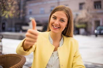 Beautiful young businesswoman showing thumb up while sitting at the cafe.