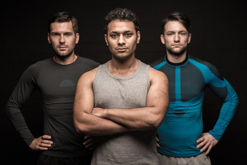 Three male friends athletes posing on black