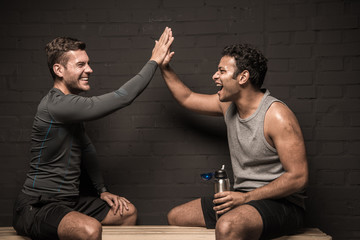 Handsome male athletes resting and conversing at gym locker room