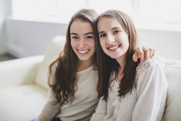 closeup portrait of hugging 2 beautiful young women having fun on sofa