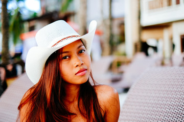 Beautiful young woman sitting on sunbed with the hat on the beach ressort, summer vacation
