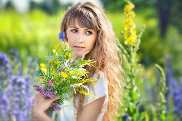 Portrait beautiful young the woman with a long fair hair who holds a bouquet of wild flowers