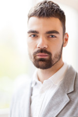 Fototapeta premium Head and shoulders portrait of handsome bearded man with deep blue eyes looking at camera while standing against blurred background