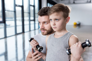 Boy training with dumbbells together with coach at fitness center
