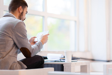 Unrecognizable bearded financial manager sitting in cozy office lobby and analyzing statistics with help of digital tablet, profile view