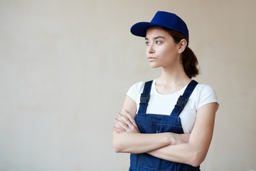Portrait of confident female construction worker against white wall background wearing blue overalls standing with arms crossed