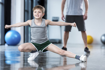 Fototapeta na wymiar Coach controlling boy that doing stretching exercise at fitness center