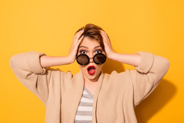 No way! Close up portrait of shocked girl in stylish sunglasses and casual wear on the yellow background