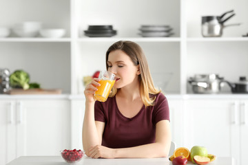 Obraz na płótnie Canvas Beautiful woman drinking fresh juice in kitchen
