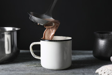 Pouring tasty cocoa into mug on wooden table against black background