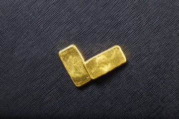 Gold bar put on the black color artificial leather surface background.