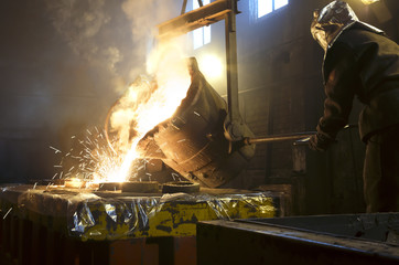 Worker controlling metal melting in furnaces. Worker operates at the metallurgical plant. The liquid metal is poured into molds.