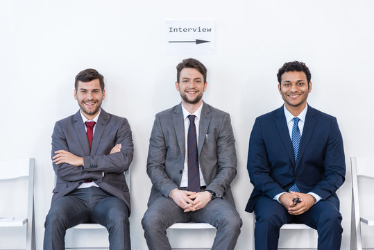 Businessmen In Suits Sitting On Chairs At White Waiting Room. Business Meeting