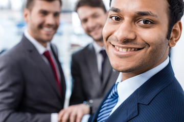 Close-up portrait of smiling african american businessman looking at camera with colleagues standing behind, business concept