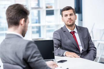 Two businessmen in formal wear sitting and talking at job interview, business concept