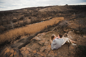 Love, romance and people concept - happy young couple hugging sitting on the edge of a cliff outdoors