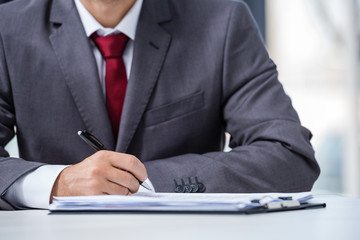 Cropped shot of businessman in formal wear signing contract at workplace, business concept