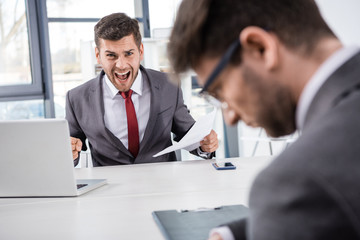 angry boss with documents shouting at upset colleague at workplace