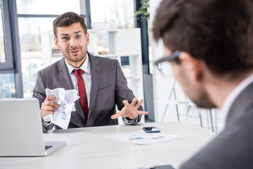 stessed boss looking at upset colleague at business meeting