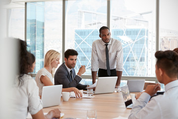 Businessman Stands To Address Meeting Around Board Table