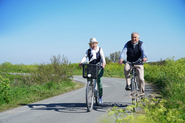 Senior couple riding bike together on country road