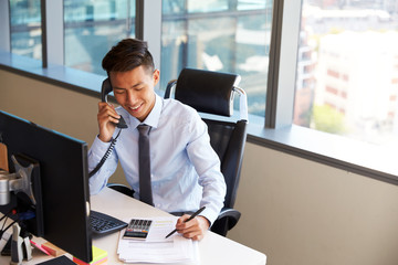 Businessman Making Phone Call Sitting At Desk In Office
