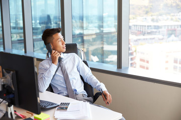 Businessman Making Phone Call Sitting At Desk In Office