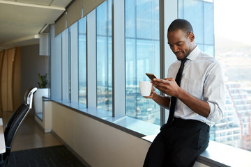 Fototapeta premium Man using phone while sitting on&nbsp;windowsill