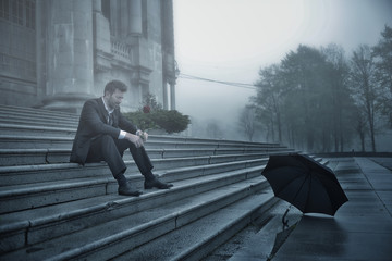 sad man sitting with rose in a foggy day