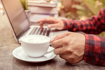 Man holding a cofffee; on table with laptop and books, vintage style.